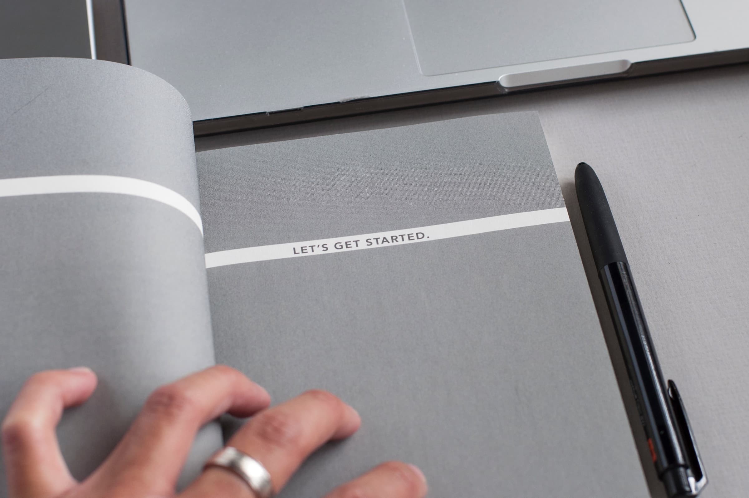Photo of a hand and pen next to a notebook with the title 'Let's Get Started'